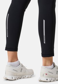 Leggings sportivi neri con dettagli riflettenti lungo i lati. Abbinati a scarpe da ginnastica bianche e calze alla caviglia bianche per un contrasto.