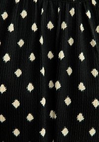 Tela negra con un patrón de diamantes blancos por toda la superficie, que presenta una textura. El diseño está distribuido de manera uniforme y es simétrico.