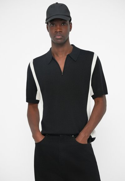 Polo negru cu mâneci scurte, cu dungi albe pe laterale, având guler cu fermoar și mâneci ribbate. Asortat cu pantaloni negri.