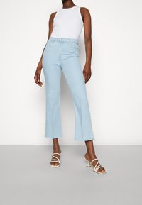 Vaaleansiniset katkotut farkut, joissa on korkeavyötärö, raakareuna ja kapea istuvuus, yhdistettyinä valkoisiin remmikenkiin, joissa on korkeat korot.