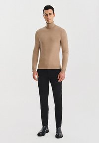 Beżowy sweter z golfem, wykonany z miękkiego materiału, dopasowany fason, ściągacz na dole, zestawiony z dopasowanymi czarnymi spodniami i czarnymi botkami.