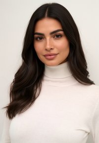 Modelo vistiendo un suéter de cuello alto blanco con textura suave, cabello largo y oscuro, y un maquillaje natural, con un fondo neutral.