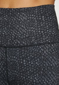 Svarta leggings med ett texturerat, reptilliknande mönster i olika nyanser av grått, med ett brett midjeband och platta sömmar för komfort.