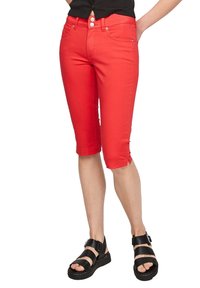 Pantalones capri de mezclilla rojos con dos bolsillos frontales, cremallera de botón y puños enrollados. Combinados con sandalias de plataforma negras con detalles de hebilla.
