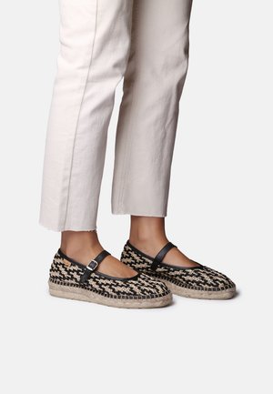 Voeten met zwarte en beige espadrilles met ruitmotief en enkelbandjes, gecombineerd met gebroken-witte cropped broeken.