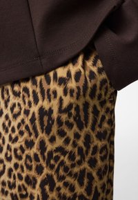 Brun sweatshirt med en slät yta ovanpå en leopardmönstrad kjol i beige och svart. Midjebandet är synligt; sydd detalj på toppen.