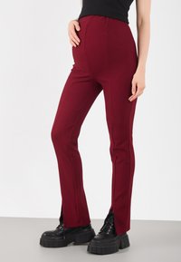 Burgundy ribbed high-waisted pants with side slits, paired with chunky black platform boots. Smooth texture with a fitted design.