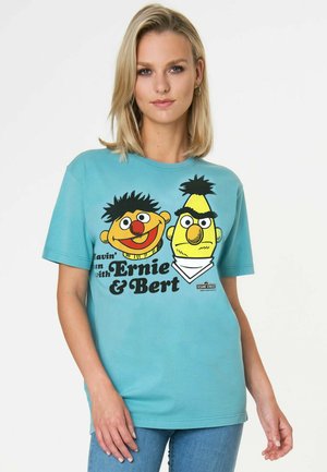 Frau trägt ein blaues T-Shirt mit bunten Ernie- und Bert-Figuren und dem Schriftzug „Havin' fun with Ernie & Bert“ von der Sesamstraße.