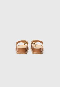 Sandales marron avec un dessus en cuir lisse, sangle de cheville ajustable et semelle plate avec des détails de couture le long du bord.