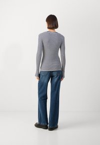 Gestreiftes Langarmoberteil in Marineblau und Weiß, kombiniert mit hochgeschnittenen blauen Jeans und schwarzen Schuhen, von hinten gesehen.