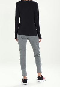 Svart långärmad topp kombinerad med ljusgrå joggers, med smalnande ärmslut och sidofickor, bärs med svarta och rosa sneakers.