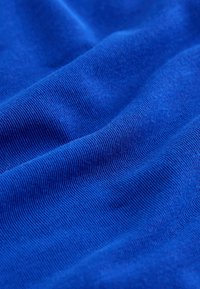 Gros plan sur un tissu bleu lisse montrant une texture fine en maille avec de doux plis et des ombres.