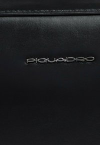 Portafoglio in pelle nera caratterizzato da una texture liscia e dal logo "Piquadro" in rilievo con finiture in argento. Design semplice con linee pulite.