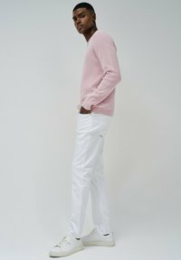 Maglione rosa lavorato a maglia, pantaloni bianchi slim-fit e sneakers bianche. L'outfit presenta un maglione testurizzato e un design pulito e minimalista.