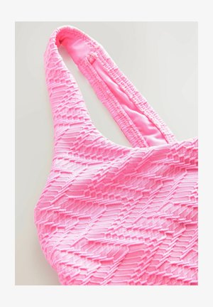 Lyserød tekstureret svømmetop med et geometrisk mønster, tynde stropper og elastiske kanter, lavet af strækbart materiale for komfort.