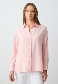 Lichtroze, lang mouwenshirt met knoopsluiting en kraag. Gemaakt van zachte stof met een losse pasvorm en een licht gebogen zoom.