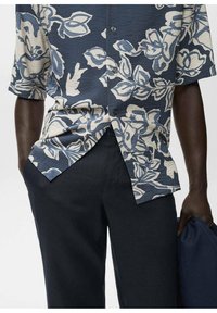 Cămașă cu mânecă scurtă, cu nasturi, de culoare bleumarin, cu un model floral crem; țesătură texturată; asortată cu pantaloni închiși la culoare; detaliu subtil al unui buzunar.