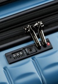 Maleta rígida de color azul claro con cremallera negra y candado combinado aprobado por la TSA. Cuenta con una superficie texturizada y dos lengüetas metálicas para tirar.