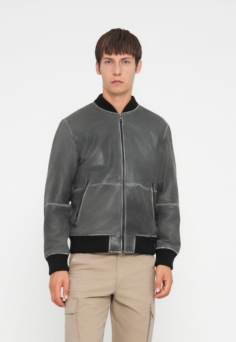 Chaqueta bomber de cuero gris con cuello y puños de canalé negros. Cuenta con bolsillos frontales y cierre de cremallera. Textura suave, diseño moderno.