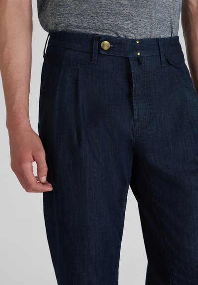 Donkerblauwe denim broek met een geplooide voorkant, voorzien van een gouden knoopsluiting en twee zichtbare zijzakken. Soepele textuur.