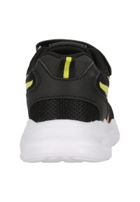Chaussure de sport noire avec une tige en mesh, dotée d'accents jaunes et d'un col rembourré. La semelle est blanche et légèrement épaissie.