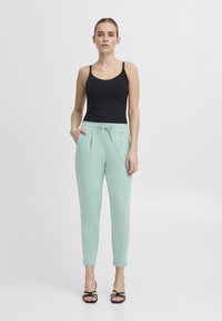 Ljust mintgröna joggers med dragsko i midjan, sidfickor och tapered bendesign, kombinerat med en svart linne och sandaler.