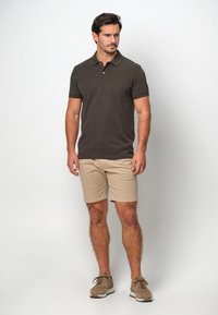 Mörkbrun polo med korta ärmar, i kombination med beiga shorts och bruna skor. Polon har en tvåknapps knäppning.