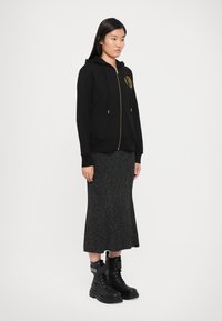 Black zip-up hoodie with gold accents, paired with a gray knitted skirt and black combat boots. Smooth fabric and relaxed fit.