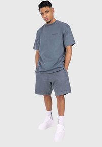 Herreoutfit med en grå bomulds-t-shirt og shorts, begge med en blød tekstur. Sammen med hvide sneakers og ankelstrømper med branddetaljer.