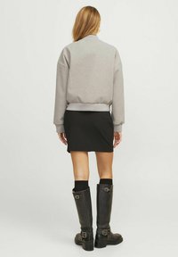 Grå sweatshirt med ribbad midja, tillsammans med en svart kjol. Knähöga svarta stövlar med spännen och en slät yta.