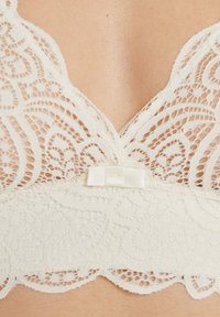 Bralette en dentelle crème avec un décolleté en V, de délicats motifs floraux et un nœud en satin au centre devant.