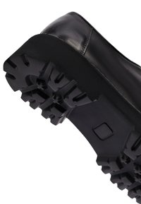 Suela de zapato de cuero negro con un taco grueso y resistente diseñado para agarre y durabilidad, mostrada desde una vista inferior en ángulo.