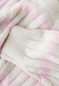 Mjuk, fluffig stickad tyg i kräm- och blekrosa ränder med ribbad struktur och veckad lagerutseende.