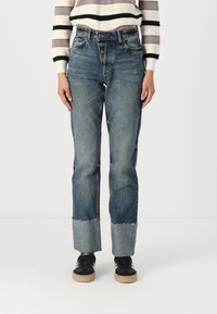 Light blue high-waisted jeans in faded denim with a straight leg, featuring a frayed hem and five-button closure, paired with black sneakers.