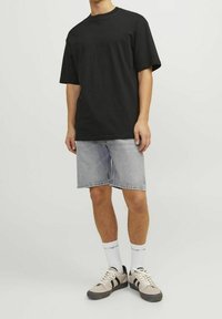 Maglietta nera in cotone a maniche corte, abbinata a pantaloncini di denim chiaro. Calzini bianchi e scarpe sportive beige con dettagli neri completano l'outfit.