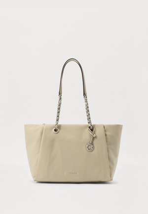 Sac cabas beige Michael Kors avec anses à maillons et breloque ronde en métal avec logo sur fond blanc.