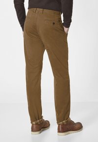 Braune lässige Hosen mit schlankem Schnitt, ausgestattet mit Gesäßtaschen und umschlagbaren Säumen. Hergestellt aus einem glatten Stoff, kombiniert mit braunen Schuhen.