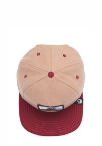 Baseball cap with a tan upper and red brim. Features a textured fabric, stitched detailing, and a logo patch on the front.