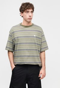 Ριγέ t-shirt σε ελιά πράσινο με οριζόντιες λευκές, γκρι και μωβ ρίγες. Διαθέτει λαιμόκοψη τύπου crew και μικρό λογότυπο στο στήθος.