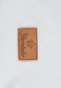 Braunes Lederetikett mit eingraviertem Text "Sterntaler" und Sternmotiv, auf einen strukturierten weißen Stoffhintergrund genäht.