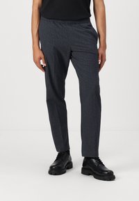 Pantalones oscuros de rayas grises para hombre con un ajuste relajado, que cuentan con una cintura elástica y una textura sutil, usados con zapatos negros de cordones.