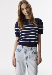 Marine gestreepte pullover met korte pofmouwen en geribbelde manchetten, gecombineerd met lichtblauwe versleten spijkerbroek. Casual outfit ontwerp.