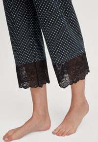 Pantaloni capri neri con pois e bordo in pizzo all'orlo. Il tessuto è liscio e il pizzo presenta un motivo floreale. Non ci sono tasche visibili.