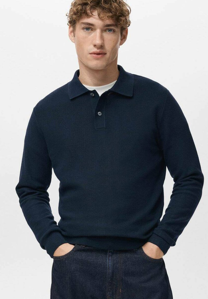 Granatowy, długi rękaw, koszulka polo z fakturowanym splotem, trzy guziki i klasyczny kołnierzyk. Noszona casualowo, z rękami w kieszeniach.