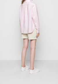 Ljust rosa och vitrandig knapp-up skjorta, långärmad, avslappnad passform, böjd nederkant, kombinerad med beige shorts och vita skor.