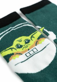 Calzini verdi con un personaggio dei cartoni animati dai grandi occhi e orecchie, contornato di nero, con un design bianco e arancione su uno sfondo contrastante.