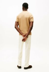 Beige kortærmet t-shirt, slim fit, parret med hvide cargo-bukser. Outfittet har en afslappet silhuet og subtil tekstur.