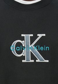 Black sweatshirt with embroidered "Calvin Klein" in turquoise and gray letters. Crew neck design; textured fabric with stitched details.