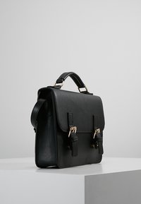 Borsa a tracolla in pelle nera con hardware dorato, patta frontale, doppie cinghie con fibbie, manico superiore e tracolla staccabile.