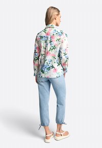 Bloemmotief blouse met lange mouwen in lichte stof, voorzien van roze en blauwe bloemen op een witte achtergrond. Gecombineerd met lichtblauwe broek.